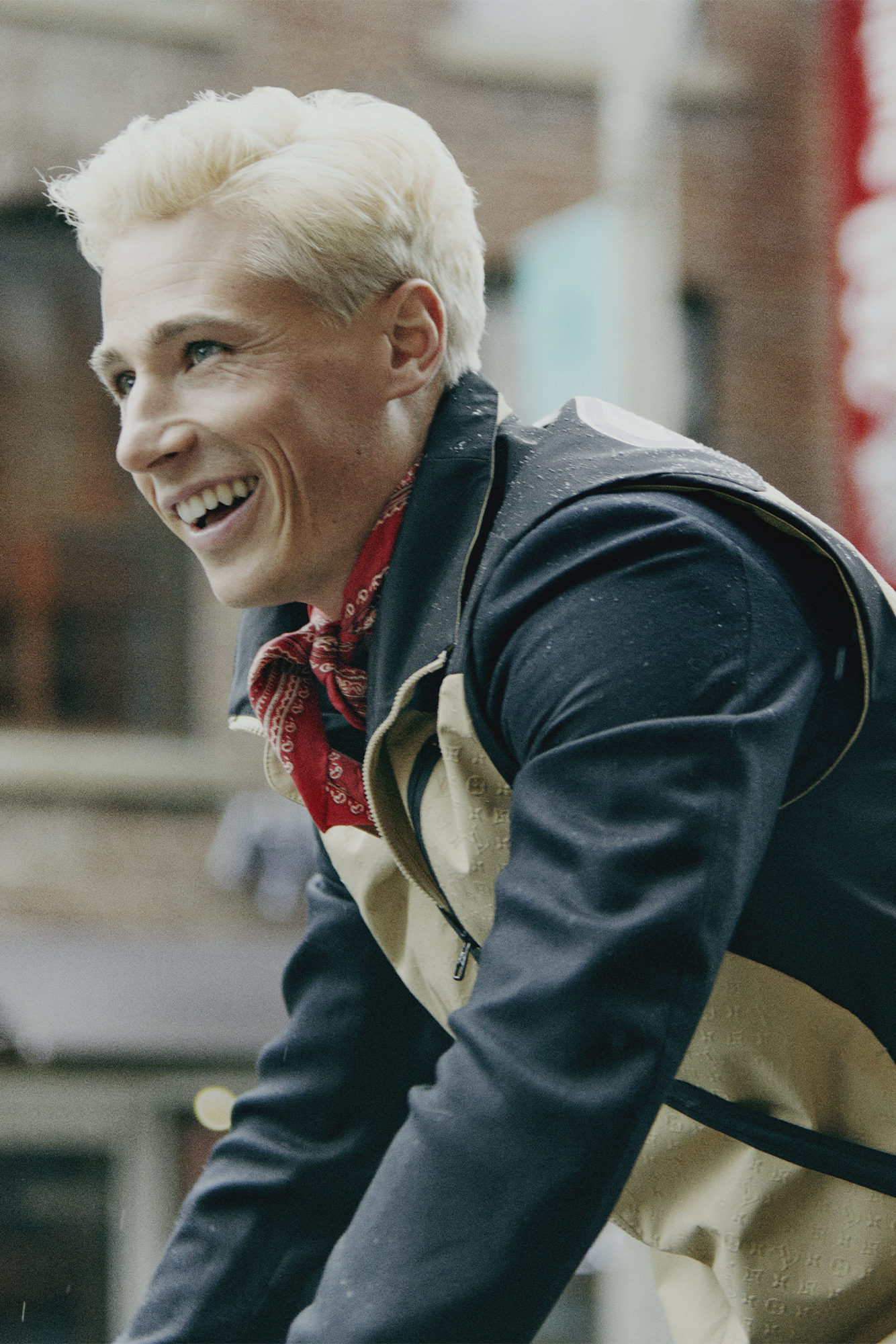 Male model in light brown and navy jacket and red handkerchief, side profile laughing and looking up