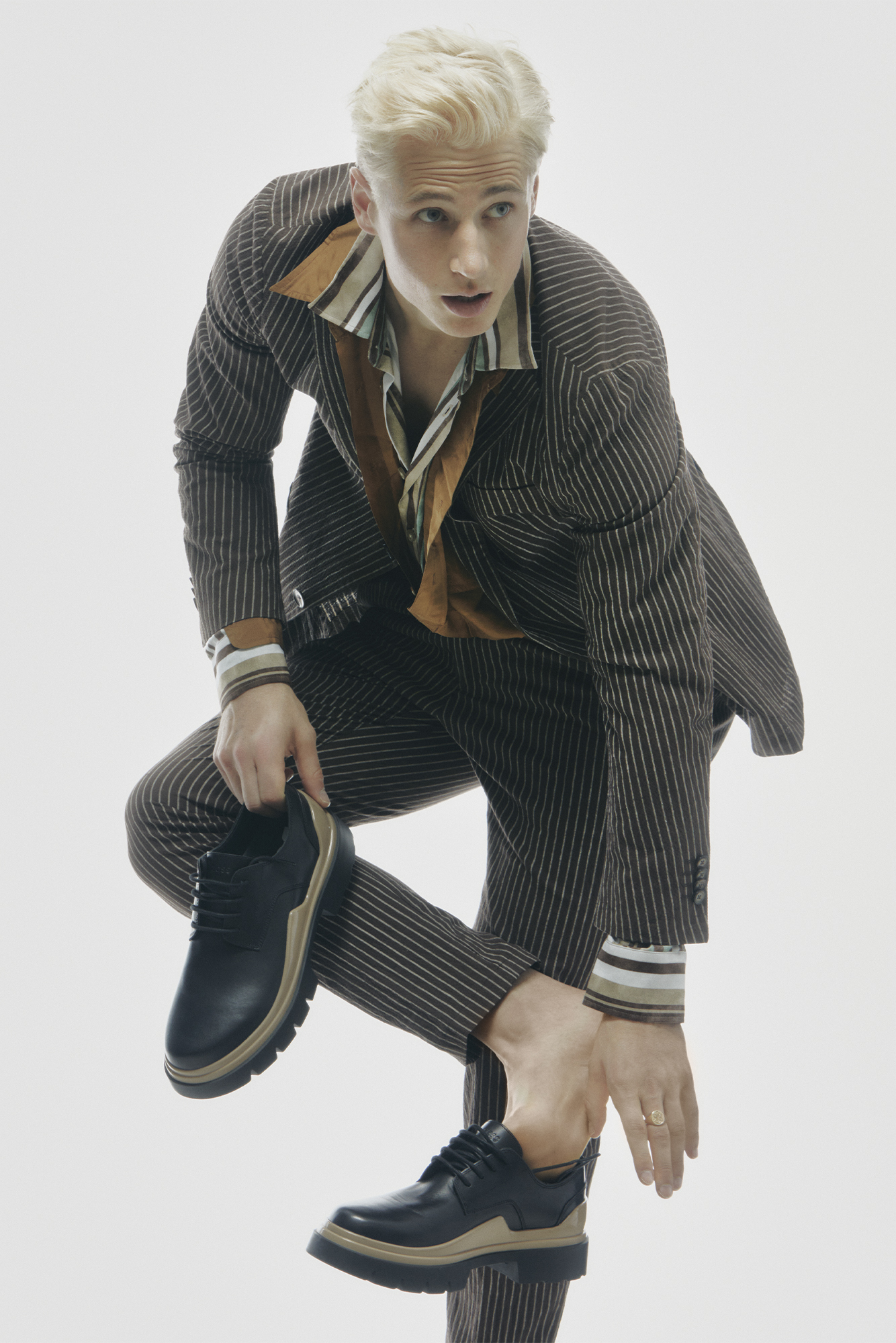 Male model in brown jacket reaching down to put on shoe while standing