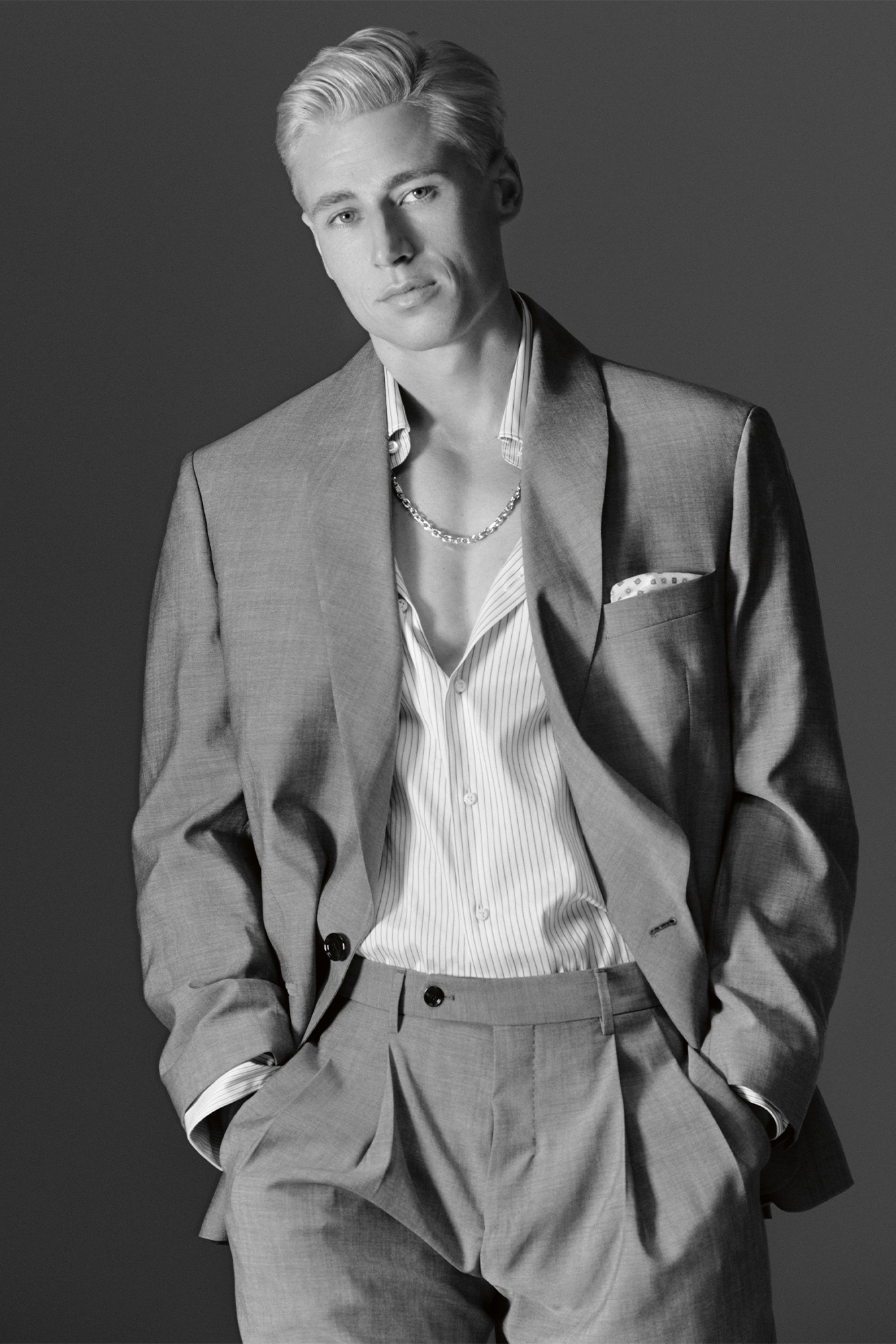 Male model in black and white with hands in suit pockets, half buttoned white shirt and suit jacket